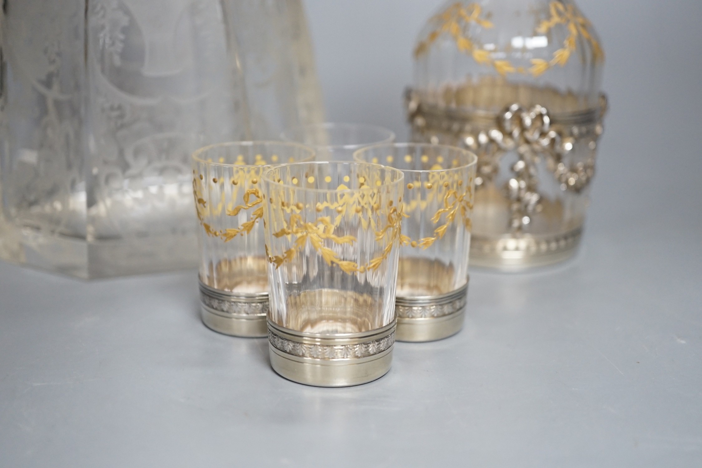 An early 20th century French white metal mounted gilded glass decanter and stopper and four matching tots, decanter height 19.7cm, and a French white metal collared etched glass decanter and stopper.